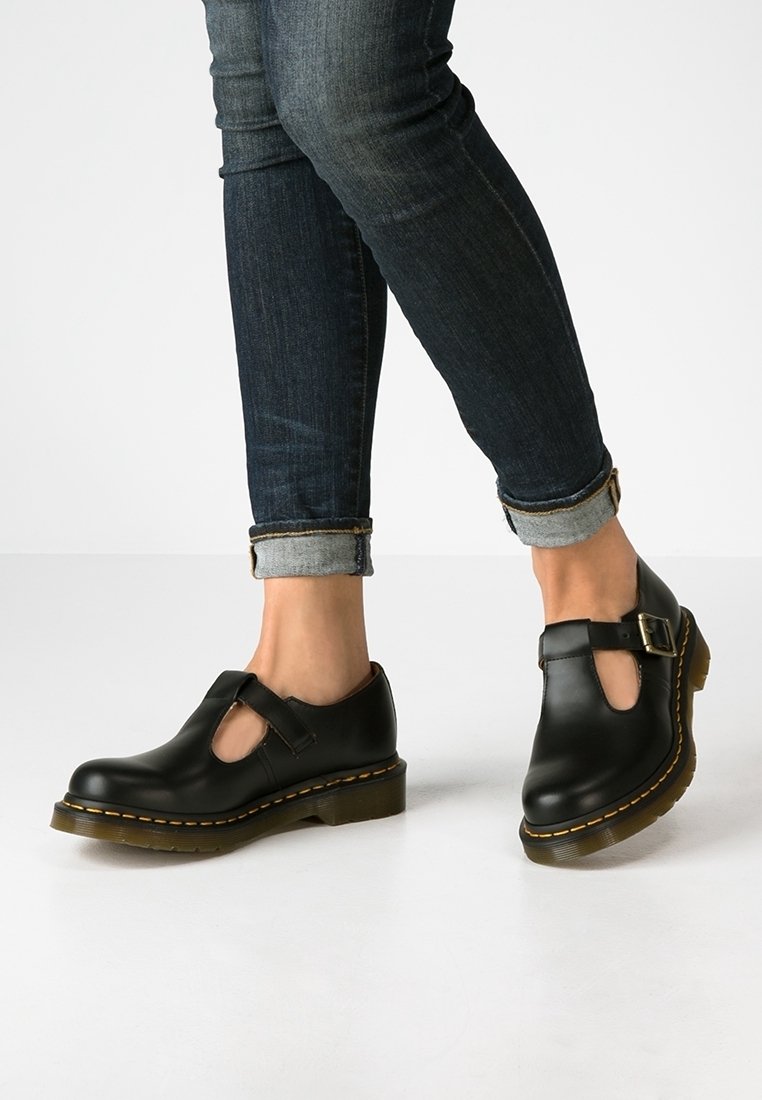 Des chaussures Mary Jane en cuir noir avec une découpe au niveau des orteils, une sangle et un détail de boucle, ainsi qu'une semelle épaisse, assorties à un jean en denim foncé.