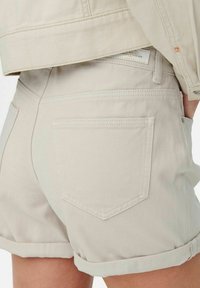 Shorts en denim beige avec un ourlet roulé, dotés de poches arrière et de coutures discrètes. Le tissu a une texture lisse et une conception robuste.