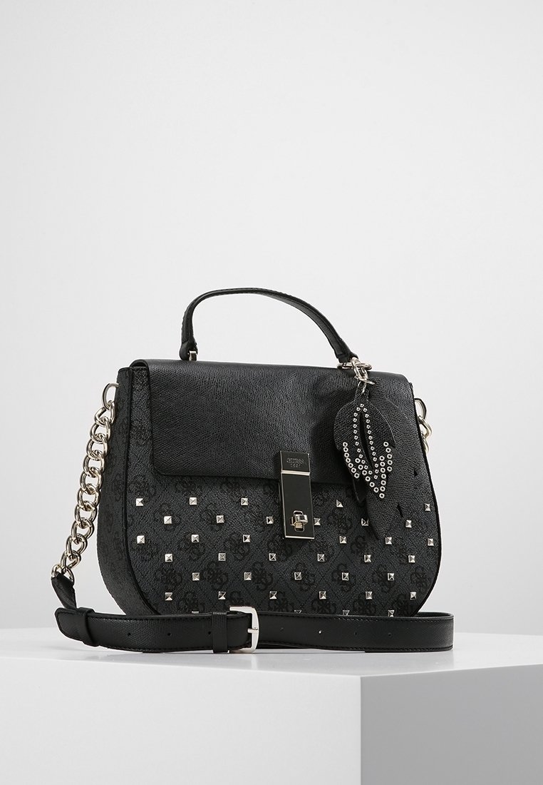 Sac à main noir en cuir texturé, avec des clous argentés, une fermeture à serrure argentée, et un pompon décoratif amovible. Comprend une bandoulière chaîne.