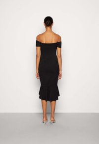 Vestido negro sin mangas con un cuerpo ajustado y un dobladillo acampanado. Tejido suave, hasta la rodilla, combinado con zapatos de tacón transparente.