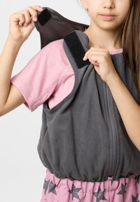 Grå fleecevest med lynlås foran og velcro skulderremme, båret over en pink skjorte. Torsoen er elastisk for en tætsiddende pasform.