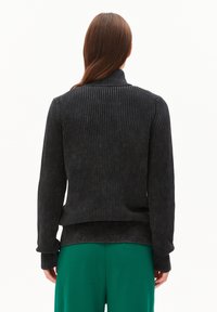 Dunkelgrauer gerippter Pullover mit langen Ärmeln und hohem Kragen, mit einem taillierten Saum und weichem Material. Kombiniert mit grünen Hosen.