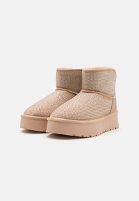 Botas de tobillo beige hechas de suave ante, con adornos de strass metálico, un forro de felpa y una suela de goma gruesa para mayor tracción.