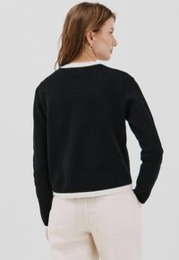 Czarny sweter dziany z białym wykończeniem przy dekolcie i dolnym brzegu, z długimi rękawami i luźnym krojem.