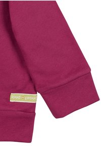 Manica di una felpa marrone che mostra una texture liscia, con un polsino e un'etichetta che recita "loud + proud" in giallo su uno sfondo bianco.