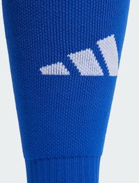 Modrá pletená ponožka s rebrovanou textúrou, ktorá má pri vrchu tri biele trojuholníkové akcenty. Dizajn zdôrazňuje pevné sedenie.