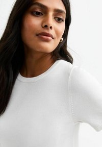 Blusa blanca de manga corta hecha de una tela suave, con un escote redondo y sutiles detalles de costura en las mangas.