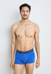 Modré boxerky vyrobené z mäkkej látky s čiernym pásom s logom GANT. Majú tesný strih a hladkú textúru.