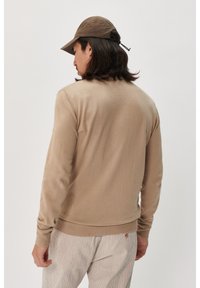 Pulover bej tricotat cu mâneci lungi, guler rotund și manșete cu nervuri. Purtați cu pantaloni ușor striați și o pălărie maroon.
