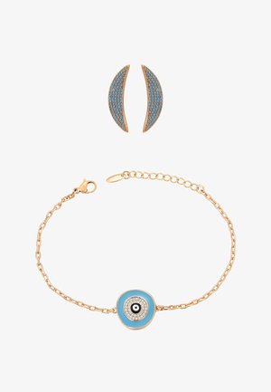 Bransoletka w kolorze złotym z niebieskim charms w kształcie oka proroka oraz dopasowane zakrzywione złote kolczyki z niebieskimi kamieniami na białym tle.