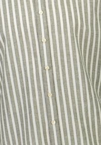 Tissu à rayures verticales gris et blanc avec une colonne centrale de six petits boutons blancs cousus en ligne.