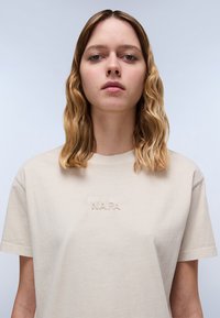 Beige katoenen t-shirt met de ingedrukte tekst "N.A.P.A." op de voorkant. Ronde halslijn en korte mouwen, gladde textuur.