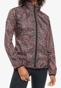 Veste à motifs floraux dans des tons de noir, rose et blanc, avec un col montant et une fermeture éclair intégrale, fabriquée en tissu lisse et léger.