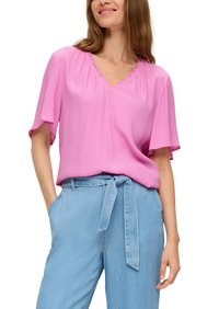 Roze blouse met korte mouwen en een V-hals, voorzien van geplooide details, gecombineerd met lichtblauwe hoge taillebroek die aan de taille is vastgebonden.