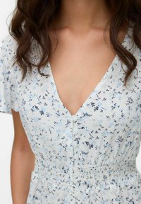 Abito floreale azzurro chiaro con scollatura a V, maniche corte e chiusura con bottoni. Il tessuto è morbido con un dettaglio in vita smock per una vestibilità migliore.
