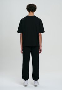 Svart oversized t-shirt och tapered byxor, tillverkade av bomull, med avslappnad passform och korta ärmar, sedd från baksidan.