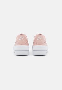 Růžové kožené tenisky s bílými podrážkami, se zvýšeným logem "NIKE AIR" na patě a hladkým povrchem.