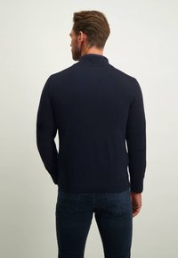Marineblauwe gebreide trui met hoge kraag, geribbelde boorden en zoom. Heeft een naadloos ontwerp aan de achterkant en een soepele textuur.