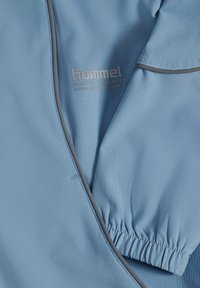 Ljusblå sportjacka i strukturerad tyg med grå detaljer. Har ett elastiskt ärmslut och broderad logotyp i en subtil design.