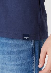 T-shirt in cotone blu navy a maniche corte, con orlo dritto e un piccolo etichetta bianca "Wrangler" vicino alla cucitura inferiore.