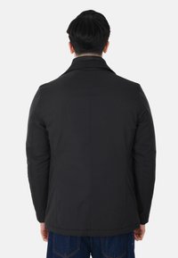 Giacca nera e imbottita con colletto, taglio dritto e maniche lunghe. Caratterizzata da una texture liscia e un design pulito e minimalista.