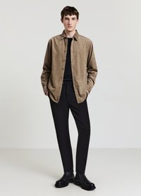 Camicia in lino marrone con chiusura a bottoni, maglietta nera a girocollo sotto, pantaloni aderenti neri e stivaletti neri. Design minimalista.