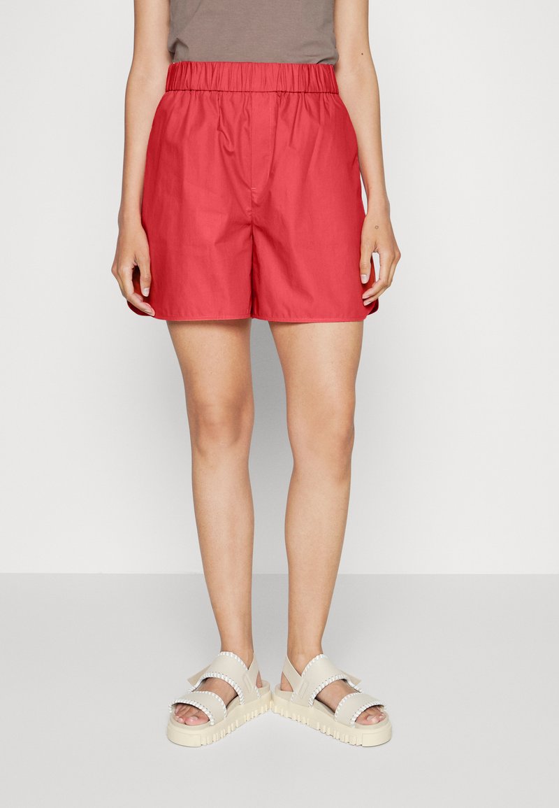 Røde bomullsshorts med elastisk midje og avslappet passform, sammen med kremfargede platåsandaler med dekorative detaljer.