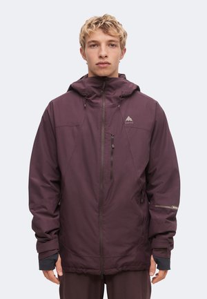 Jeune personne portant une veste à capuche violet foncé avec fermeture éclair à l'avant et poche poitrine, debout face à l'avant sur un fond uni.