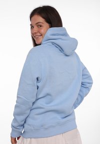 Haut à capuche bleu clair avec une coupe décontractée, des manches longues et un cordon de serrage à la capuche. Décoré de poignets et d'un ourlet côtelés, avec une texture douce.