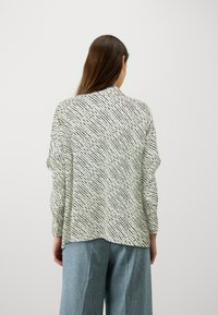 Løs passform bluse i et lett stoff, med et svart-hvitt abstrakt mønster, lange ermer og buet søm.