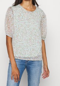 Jasnoniebieska bluzka z krótkimi puff袖ami, zdobiona kwiecistym wzorem w odcieniach różu i brązu, z okrągłym dekoltem. Teksturowany, lekki materiał.