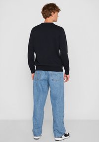 Tengerészkék pulóver kerek nyakkivágással, világoskék, bőszárú farmerral viselve. A szettet fekete-fehér tornacipő egészíti ki. Minimalista dizájn és textúra.