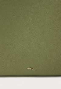 Žalios odos rankinė su tekstūruotu paviršiumi ir auksiniais metaliniais elementais, ant kurių apačios pažymėtas „FURLA“ prekės ženklas. Stačiakampio formos su minkštu išvaizda.