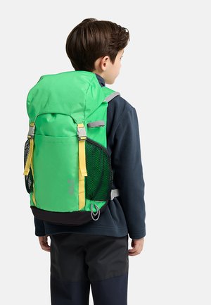Enfant portant une veste et un pantalon foncés, portant un sac à dos vert vif et jaune avec des poches latérales en filet, vu de profil sur fond blanc.