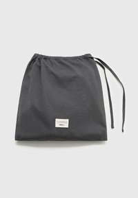 Drawstring storage bag in dark gray fabric with a smooth texture and a small labeled patch. Features a gathered top and functional ties.