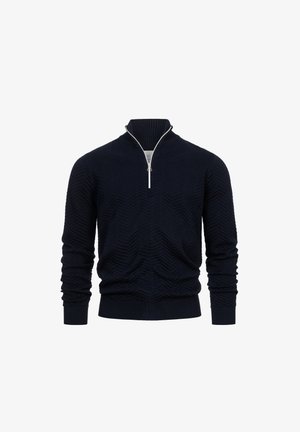 Tengerészkék zipzáras kötött pulóver, mellyel textúrált cikk-cakk minta, magas nyak és bordázott mandzsetta található, ezüst színű cipzárral.