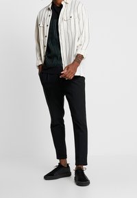 Hvid skjorte med sorte striber, lagd over en sort stribet T-shirt. Sorte tapered bukser og sorte sneakers.
