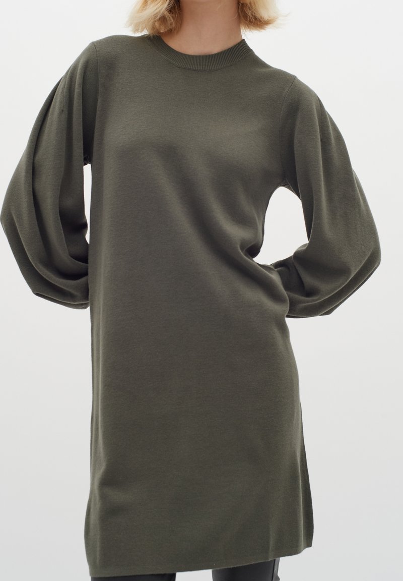 Olivgrön oversized stickad klänning med långa, lösa ärmar, ribbad halsringning och rak skärning. Mjuk textur, minimalistisk design.