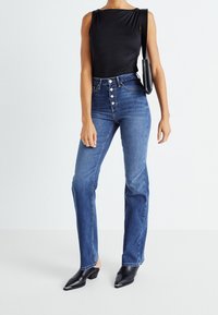 Body noir sans manches associé à un jean bleu taille haute avec un devant à cinq boutons, porté avec des mules noires à talons et un petit sac.