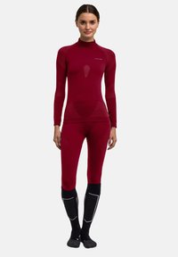 Tuta termica rossa a maniche lunghe con collo alto, trama a coste e design aderente, abbinata a calzini neri al ginocchio con dettagli grigi.