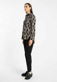 Czarna bluzka z wzorem łańcucha, z długimi rękawami i kołnierzykiem, w połączeniu z czarnymi wąskimi spodniami i platformowymi loafersami. Minimalistyczne tło.