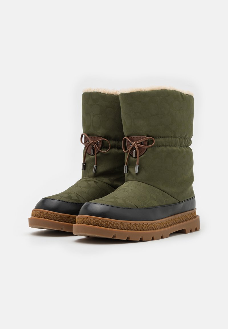 Zielone pikowane buty z czarnym gumowym noskiem, brązowym sznurowadłem i ciepłym futrzanym wykończeniem. Teksturalna podeszwa zapewnia przyczepność i stabilność.