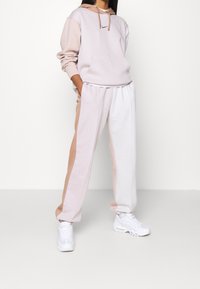 Ljusrosa hoodie med en framficka och dragsnören, i kombination med ljusa och beige mönstrade joggers; bärs med vita sneakers.