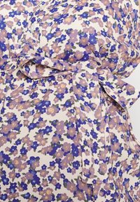 Vestido floral com um fundo creme. Apresenta flores roxas, azuis e amarelas, um laço na cintura e um design com botões. Textura de tecido suave.