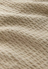 Tissu beige avec une texture en nid d'abeille, présenté en plis doux et en gros plan.