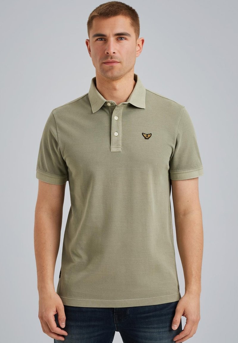 Polo en vert olive, fabriqué en coton, doté d'une patte de boutonnage à trois boutons, de manches courtes et d'un logo brodé sur la poitrine.