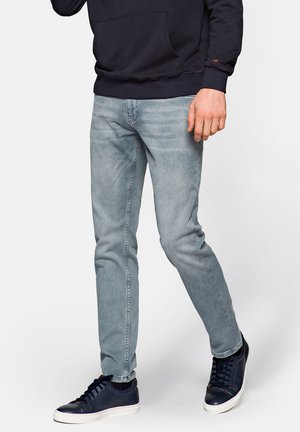 Jasnoszare jeansy slim fit z wyblakłą strukturą i subtelnym wyżłobieniem. Noszone z ciemnymi trampkami i pasującą granatową bluzą z kapturem.