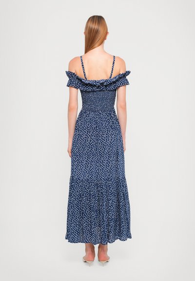 Marineblauwe off-shoulder jurk met volants aan de mouwen, gerimpelde corsage en witte stippen; vloerlange jurk met een gelaagde zoom.