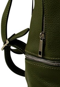 Donkergroene, textuur minder leer, rugzak met een zilverkleurige rits en een verstelbare schouderriem, gedeeltelijk zichtbaar tegen een witte achtergrond.