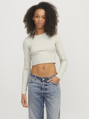 Crop top grigio chiaro con maniche lunghe, realizzato in tessuto a coste. Abbinato a jeans larghi in denim chiaro con chiusura a bottone e tasche.